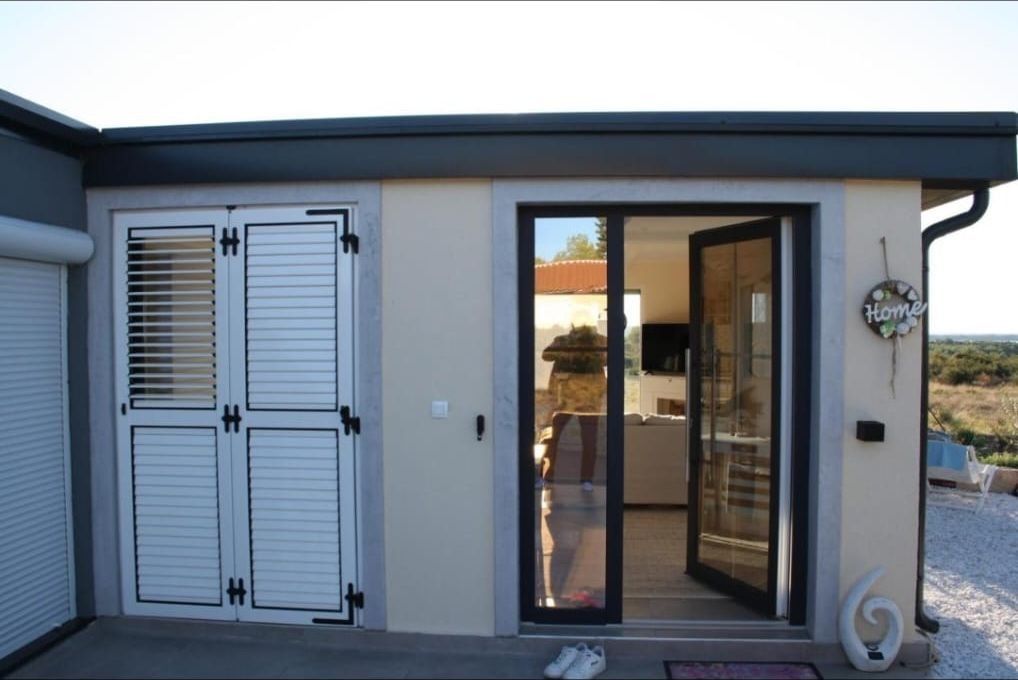 Hauseingang mit Glastür und weißen Fensterläden